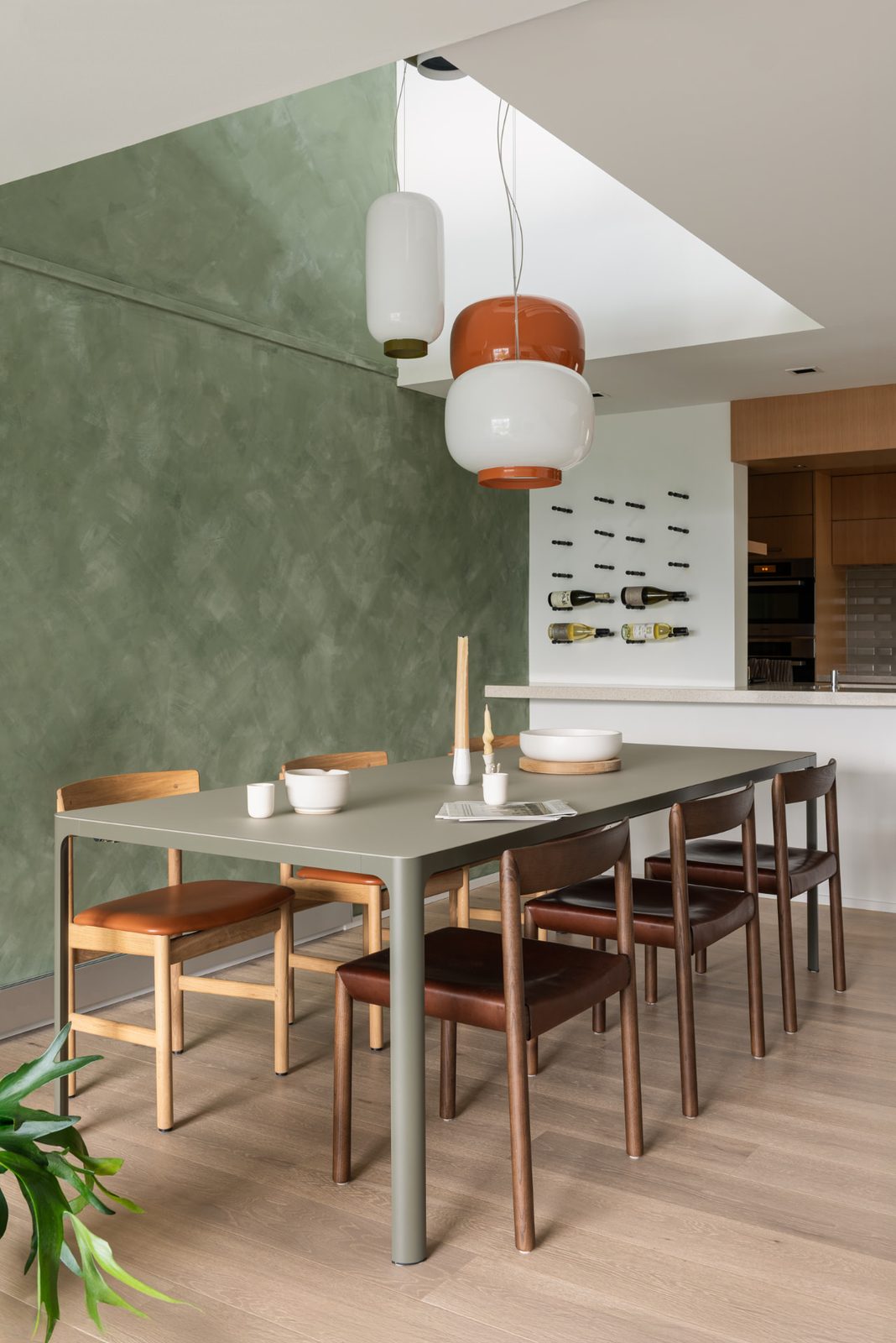 A dining room with a green plaster wall, a long table and a wine rack on the wall beyond