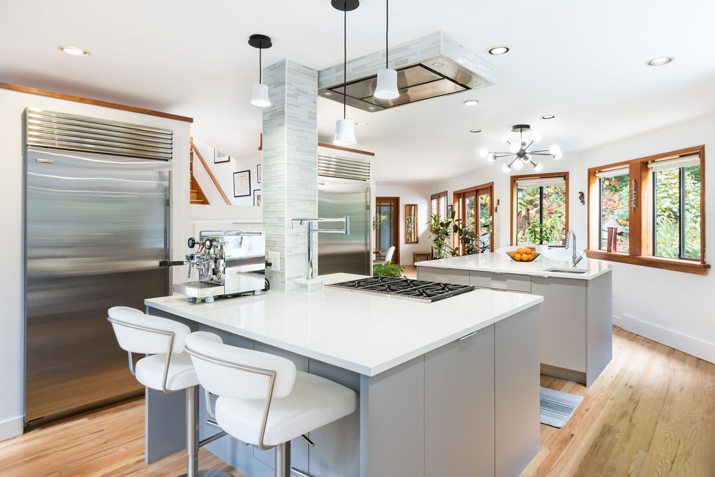 A kitchen with two islands, a cooktop under a flush ceiling hood and full height fridges