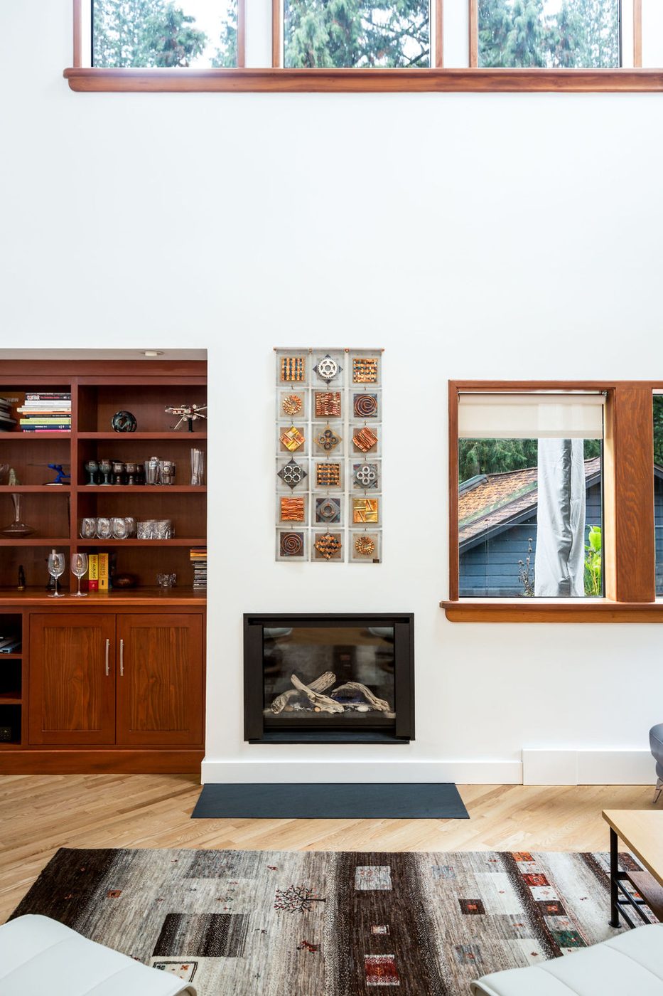 A double height living room with built in cabinetry beside a fireplace and clerestory glazing